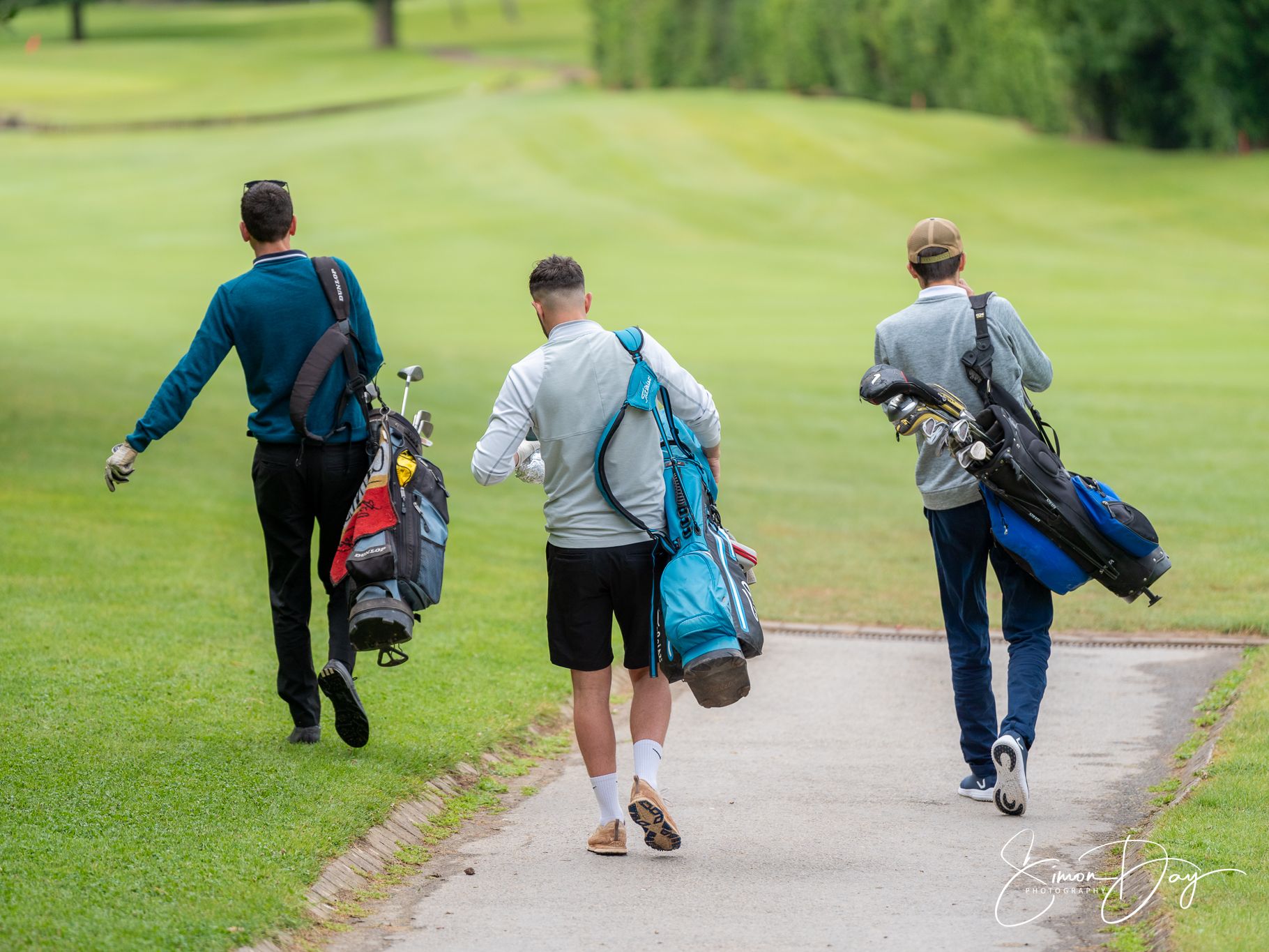 Three men walking on a golf course carrying golf bags.