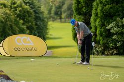 Man putting on a golf green next to a yellow sign that reads 'co create architects.'