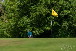 Golfer preparing to chip onto the green near a yellow flag on a sunny day