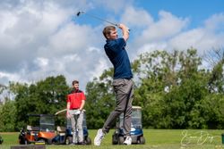 Man taking a golf swing with another person watching, golf carts in the background