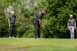 Three men on a golf course, one putting while the others look on.