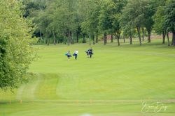 Group of golfers walking on a green golf course surrounded by trees
