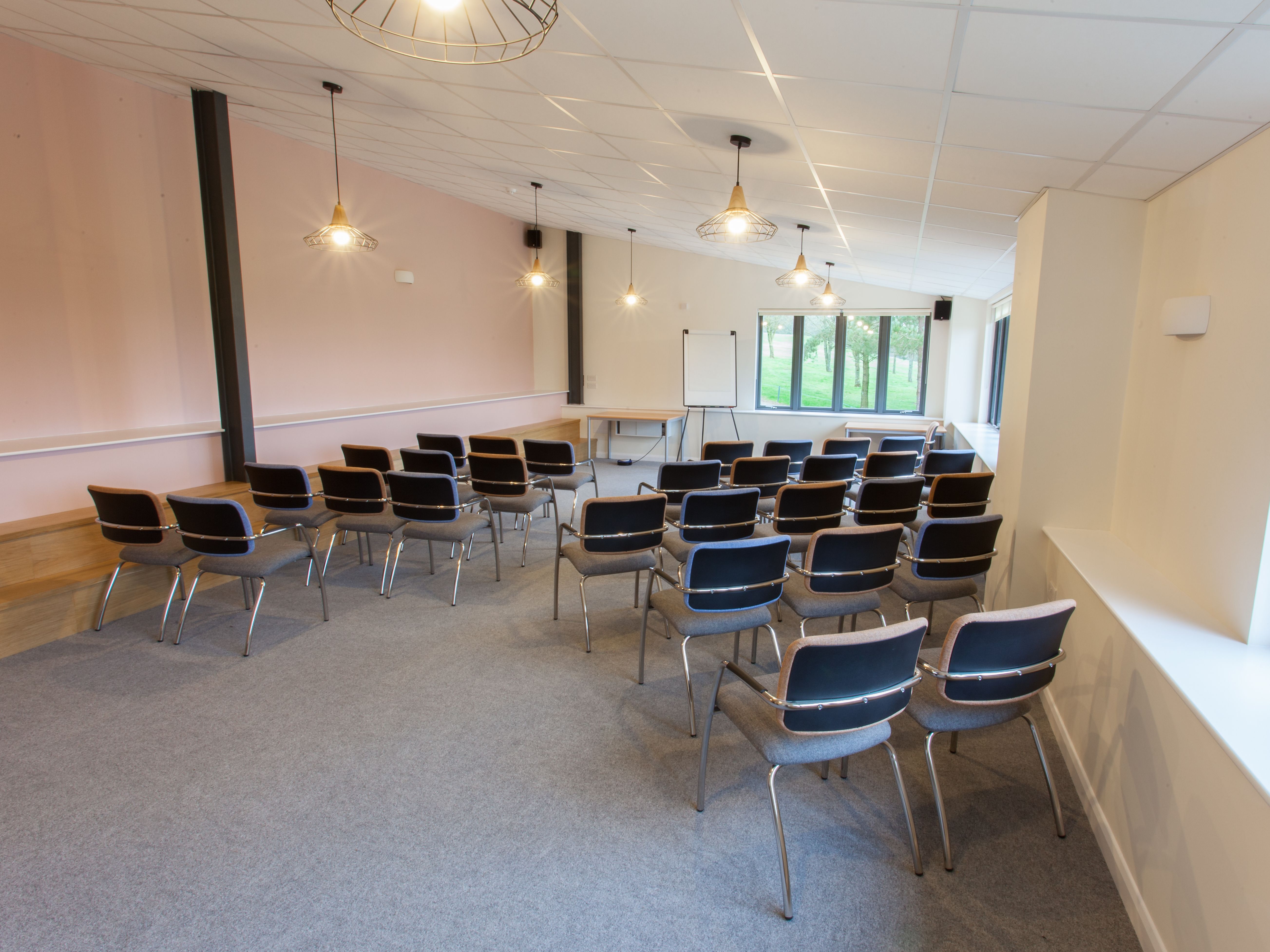 Empty conference room with rows of chairs facing a whiteboard and windows.