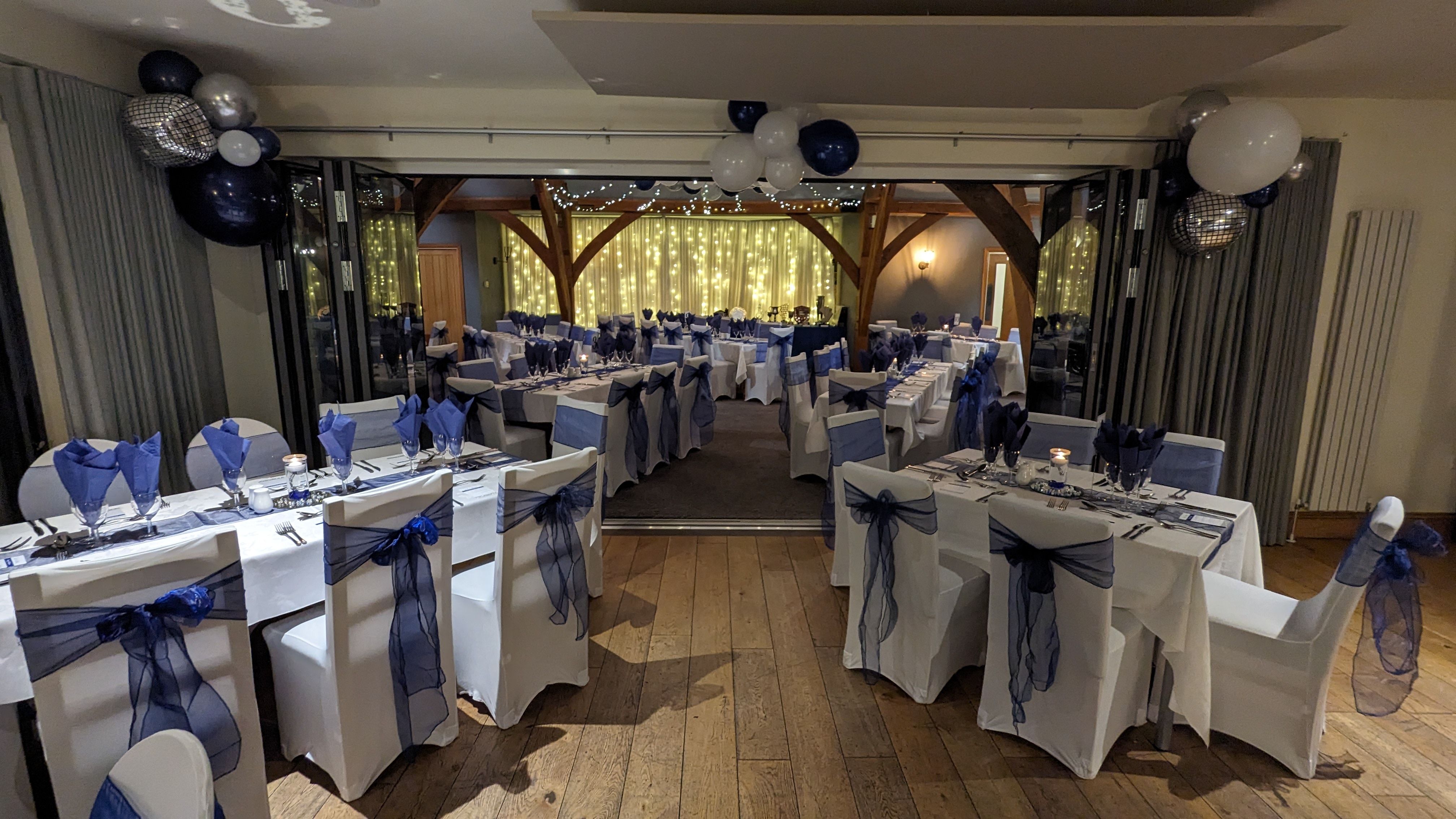 Formal banquet hall set up for an event with white tablecloths, blue decorations, and fairy lights.