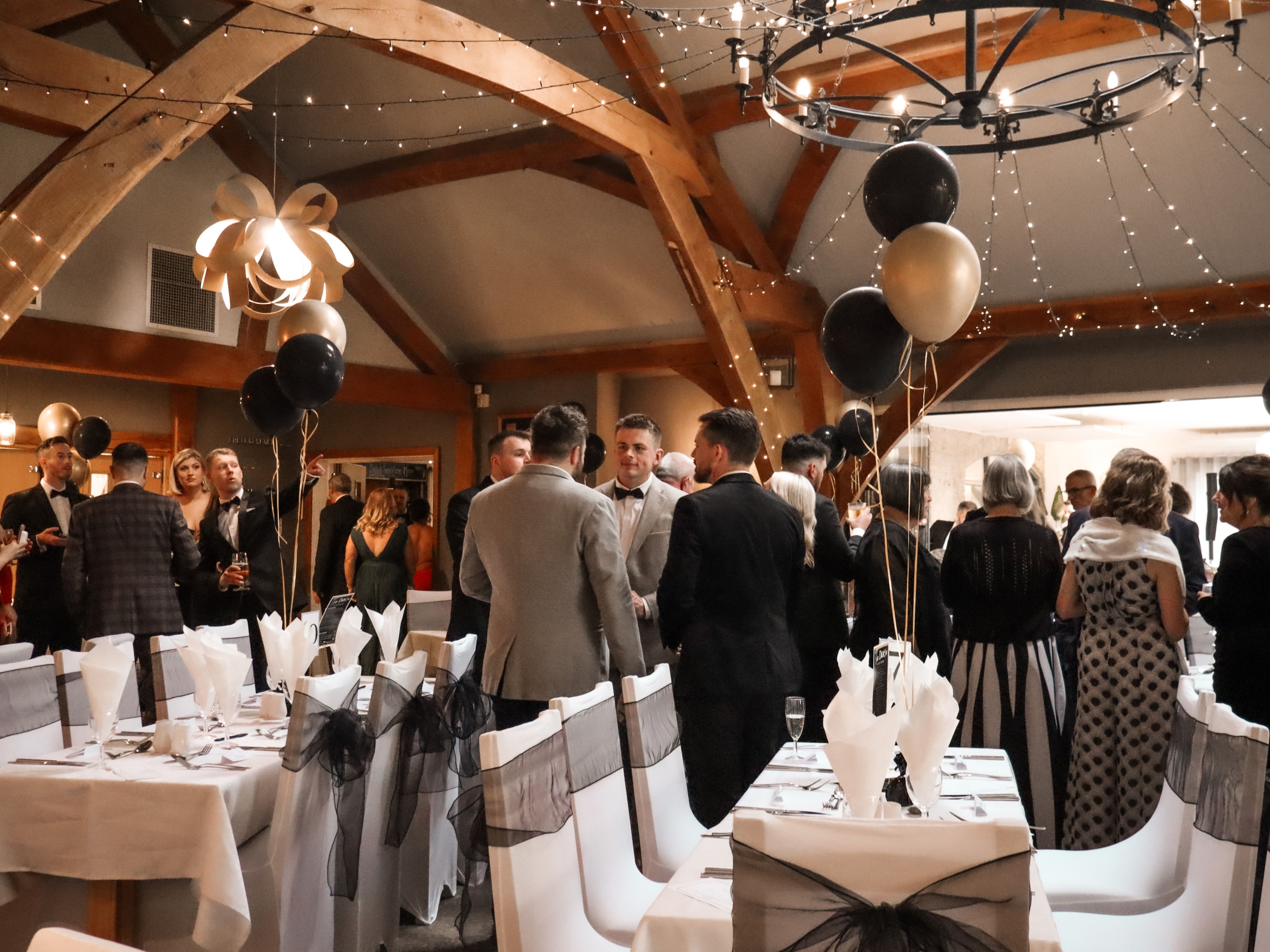 People dressed formally at a banquet or gala event with decorated tables, balloons, and festive lighting.