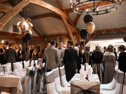 People dressed formally at a banquet or gala event with decorated tables, balloons, and festive lighting.