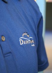 Close-up of a blue polo shirt with the embroidered logo 'Dainton Park' and a foot design.
