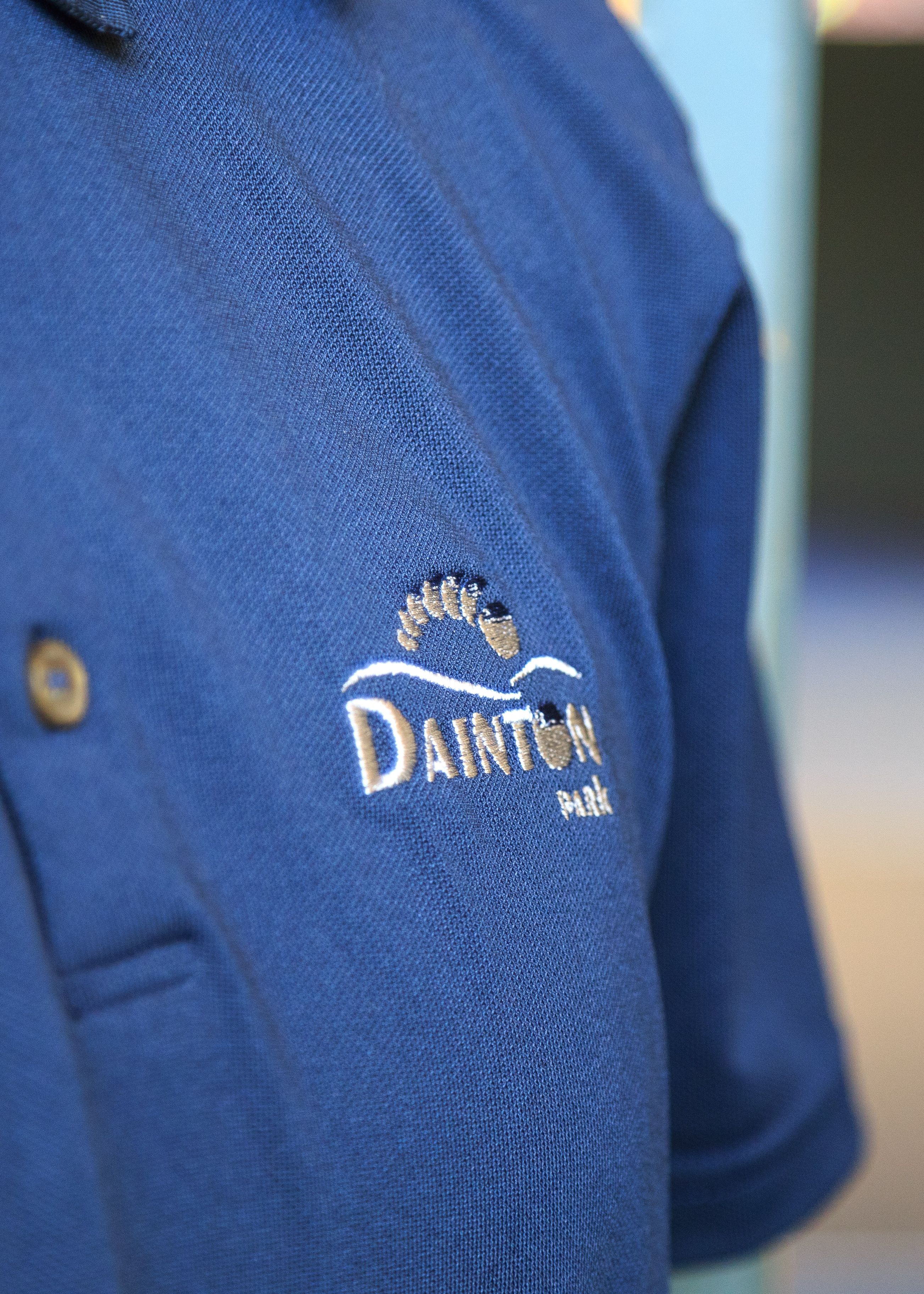 Close-up of a blue polo shirt with the embroidered logo 'Dainton Park' and a foot design.