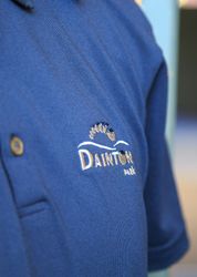 Close-up of a blue polo shirt with the embroidered logo 'Dainton Park' and a foot design.
