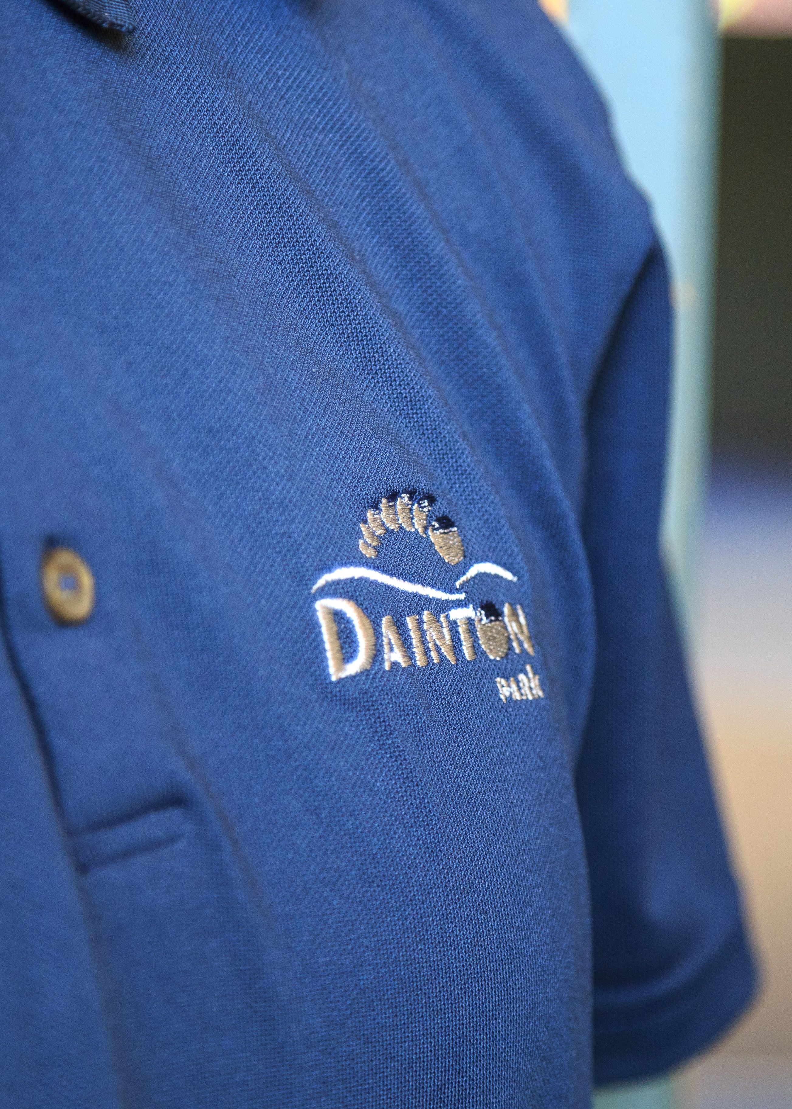 Close-up of a blue polo shirt with the embroidered logo 'Dainton Park' and a foot design.