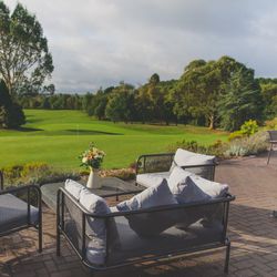 Outdoor seating area overlooking a lush green golf course with trees in the background.