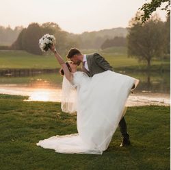 Groom dipping bride for a kiss outdoors at sunset near a pond
