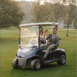 Bride and groom riding in a golf cart on a grassy field