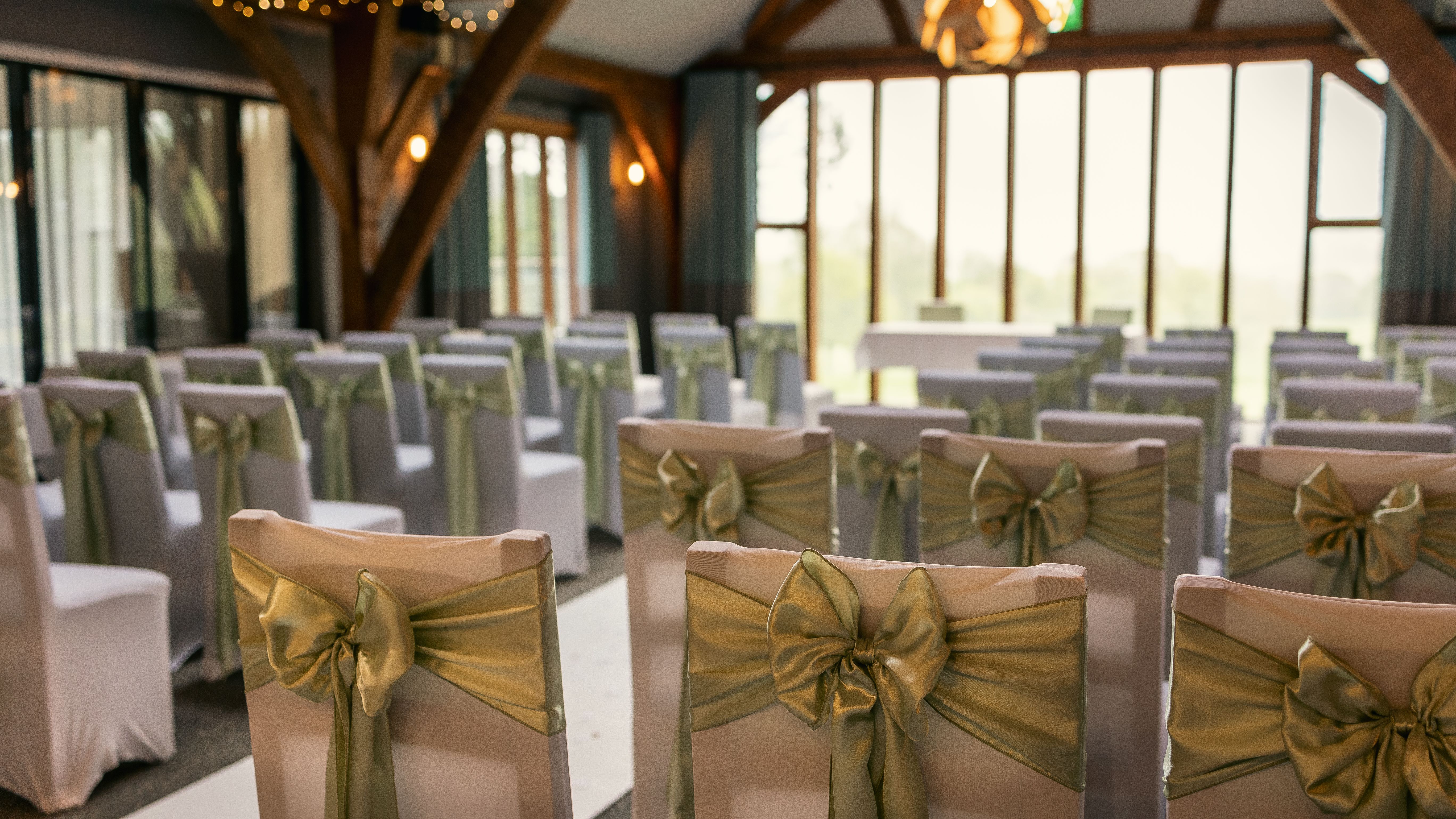 Rows of white chairs decorated with green bows in a wedding ceremony venue.