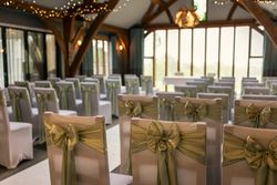 Rows of white chairs decorated with green bows in a wedding ceremony venue.