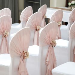 Rows of white chairs with pale pink fabric and flower decorations, arranged for an event