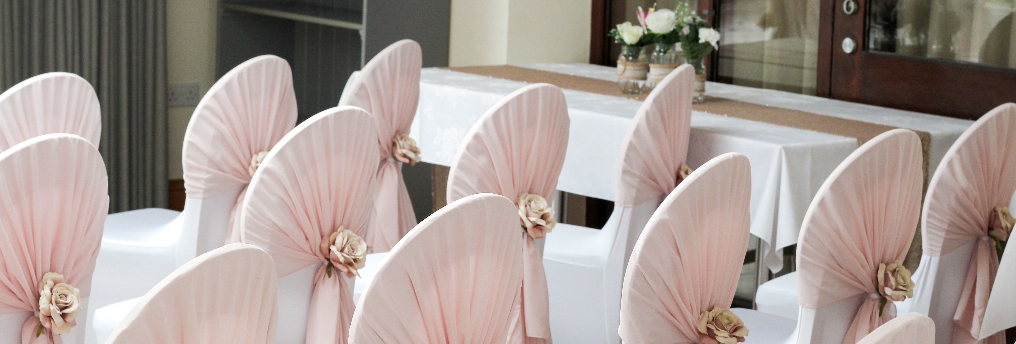 Rows of white chairs with pale pink fabric and flower decorations, arranged for an event