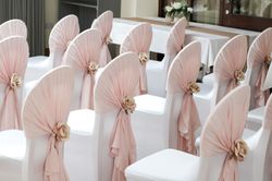 Rows of white chairs with pale pink fabric and flower decorations, arranged for an event