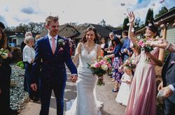 Bride and groom walking down an outdoor aisle, smiling, surrounded by guests throwing confetti.