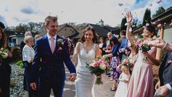 Bride and groom walking down an outdoor aisle, smiling, surrounded by guests throwing confetti.