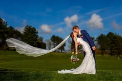 Bride and groom sharing a romantic kiss outdoors, with the bride's veil flowing in the wind.