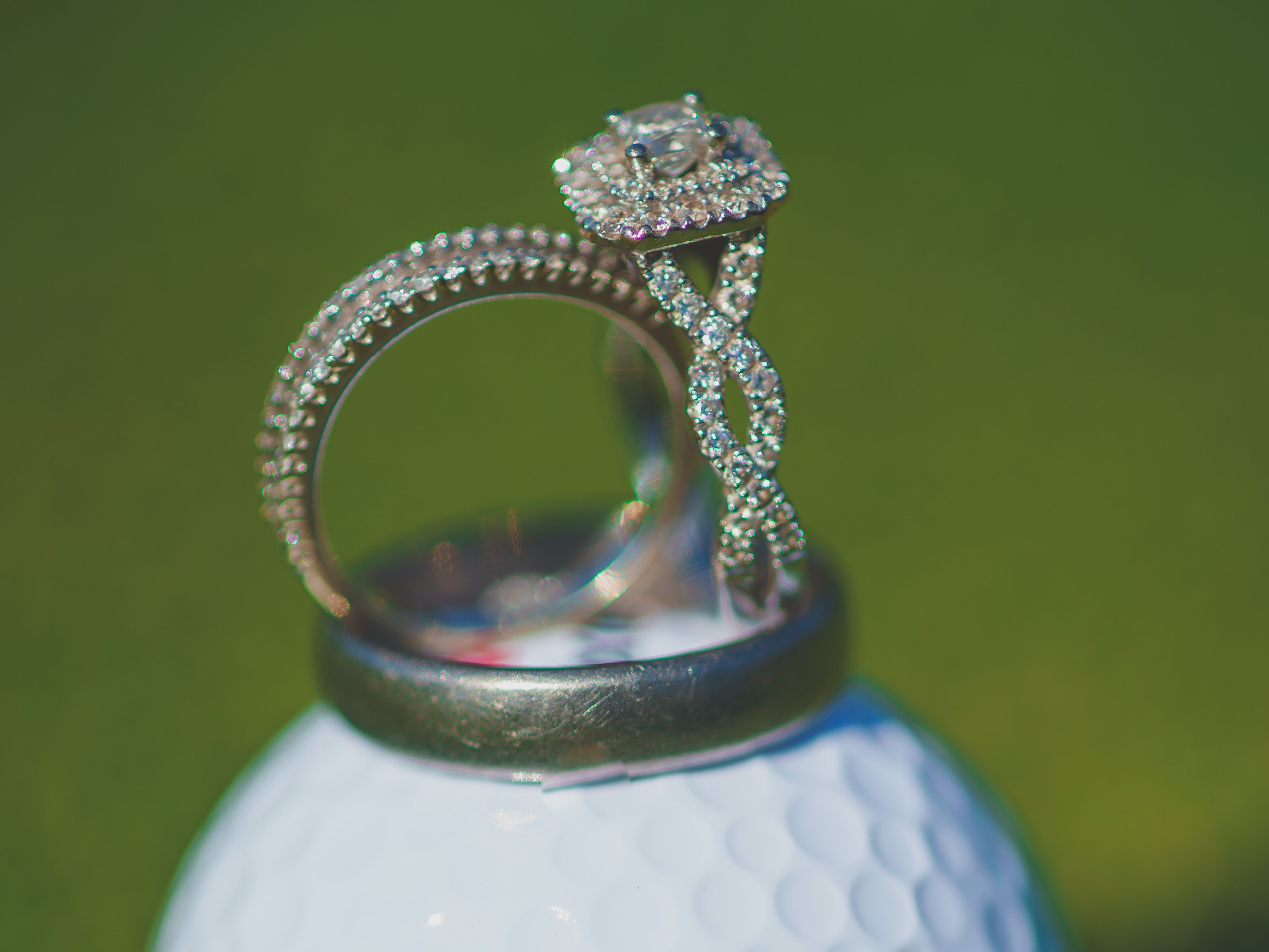 Diamond engagement ring and wedding band placed on a white Dainton Park golf ball on green grass.