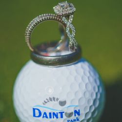 Diamond engagement ring and wedding band placed on a white Dainton Park golf ball on green grass.