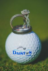 Diamond engagement ring and wedding band placed on a white Dainton Park golf ball on green grass.