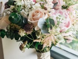 Bridal bouquet with pale pink roses, peonies, and assorted greenery on a windowsill