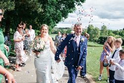 A bride and groom smiling and walking hand in hand as guests throw confetti at them outdoors.