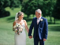 Bride and groom holding hands outdoors, smiling at each other on a sunny day.