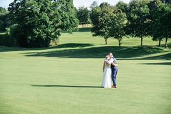 Bride and groom embracing on a sunny, green open field with trees in the background