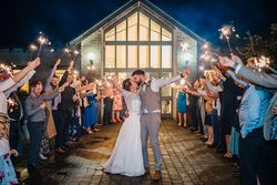 Bride and groom kissing with sparklers held by guests forming an archway outside a venue at night