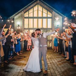 Bride and groom kissing with sparklers held by guests forming an archway outside a venue at night