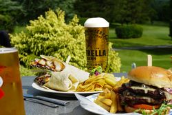 Outdoor table with a chicken wrap, burger, fries, potato chips, and Estrella Damm beer