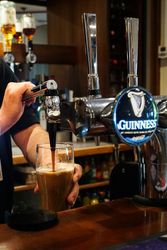 A person pouring a pint of Guinness beer from a tap at a bar.