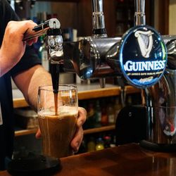 A person pouring a pint of Guinness beer from a tap at a bar.