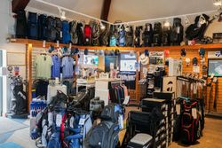 Golf pro shop interior with golf bags, clubs, apparel, hats, and accessories displayed for sale.