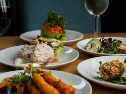 Assorted gourmet appetizers on white plates accompanied by glasses of red and white wine on a wooden table.
