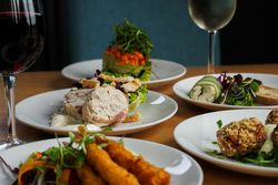 Assorted gourmet appetizers on white plates accompanied by glasses of red and white wine on a wooden table.