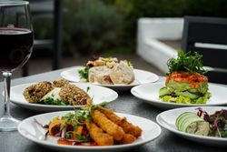 A selection of assorted gourmet appetizers on white plates, accompanied by a glass of red wine, arranged on a dark outdoor table.