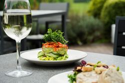 A glass of white wine and a fresh salad with greens and vegetables served on a white plate, set on an outdoor restaurant table.