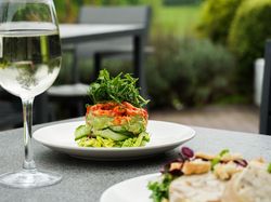 A glass of white wine and a fresh salad with greens and vegetables served on a white plate, set on an outdoor restaurant table.