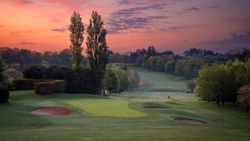Golf course at dawn with sand bunkers and trees under a colorful sky