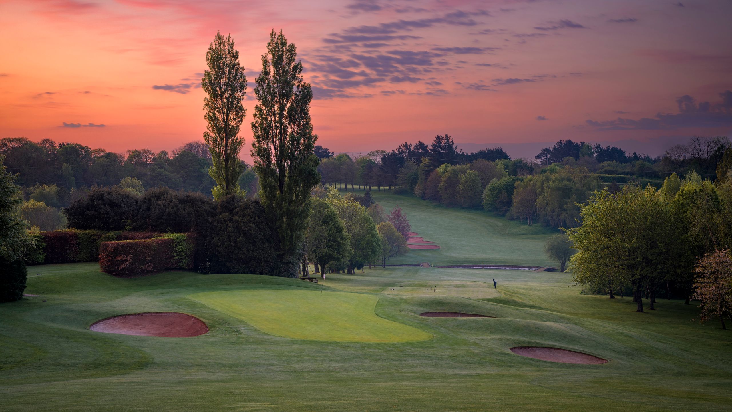 Golf course at dawn with sand bunkers and trees under a colorful sky