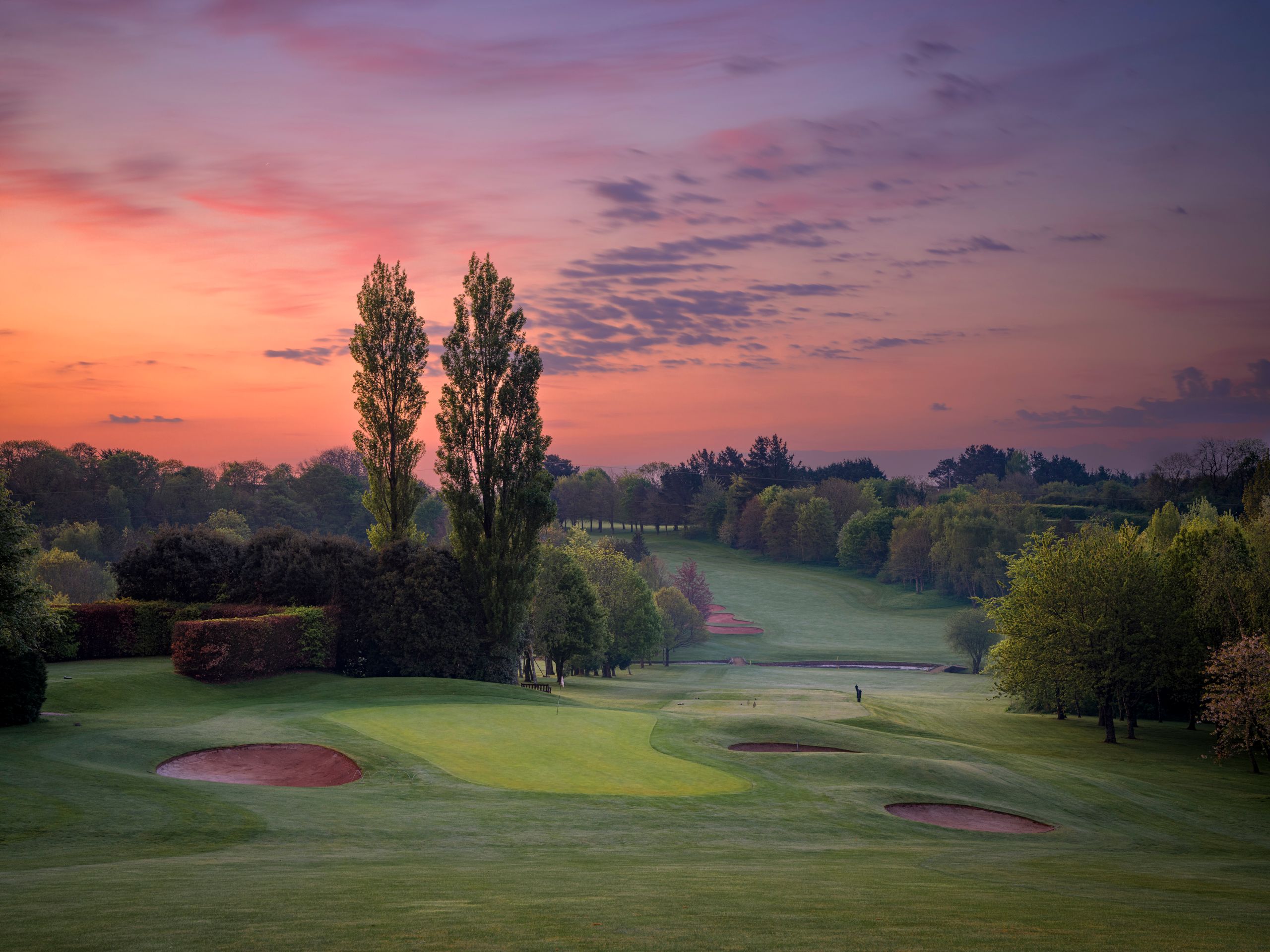 Golf course at dawn with sand bunkers and trees under a colorful sky