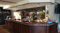 A cozy bar with a wooden counter, various bottles, glasses, beer taps, and a menu board above.
