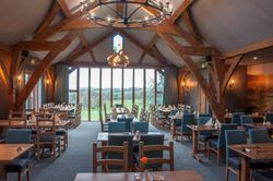 Cozy restaurant dining area with wooden beams, large windows, and tables set for guests