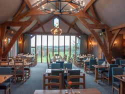 Cozy restaurant dining area with wooden beams, large windows, and tables set for guests