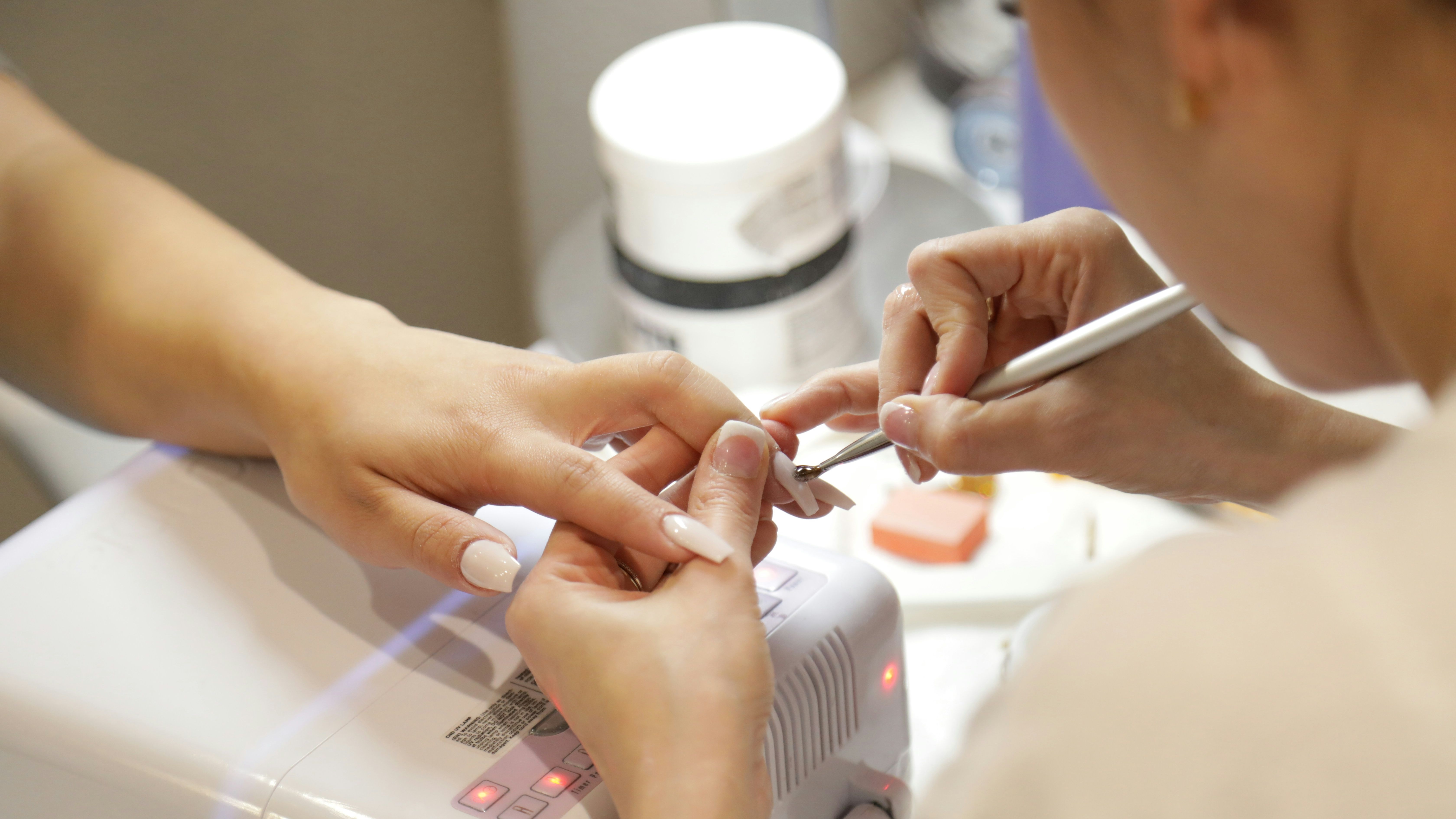 Close-up of a person receiving a manicure with a nail technician working on their nails.